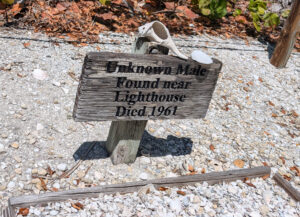Wooden grave marker with seashells in Sanibel, Florida reading ‘Unknown Male Found Near Lighthouse Died 1961’ in a sandy setting